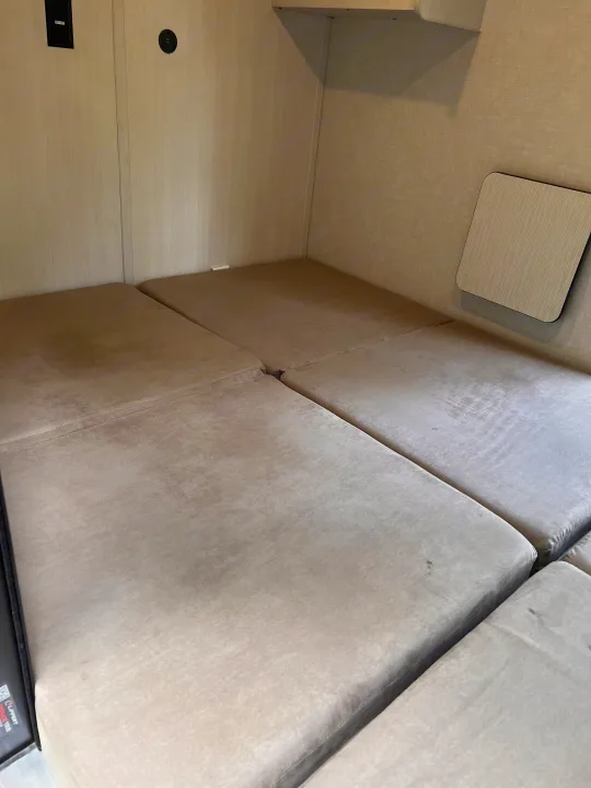 RV rental bed area with light-colored upholstered cushions, wall paneling, and charging ports. A small table is on the right.. Forest River NoBo 10.7 2024