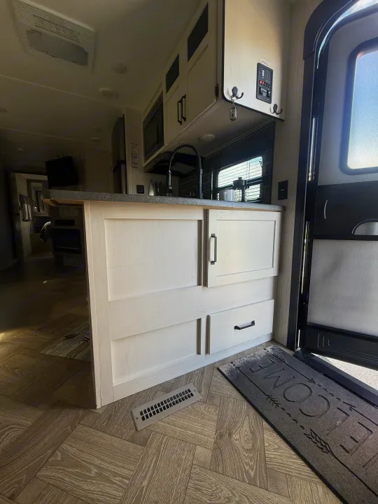 Modern RV rental kitchen featuring light wood-look cabinetry, dark countertops, and a welcome mat by the entrance.. Forest River Palomino Puma 2022
