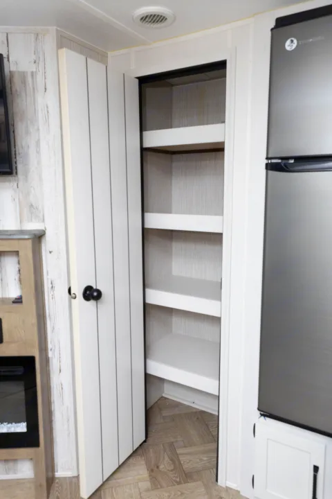 Spacious RV rental kitchen pantry, open to reveal multiple shelves. A refrigerator is on the right, in a bright, modern interior.. Forest River Palomino Puma 2022
