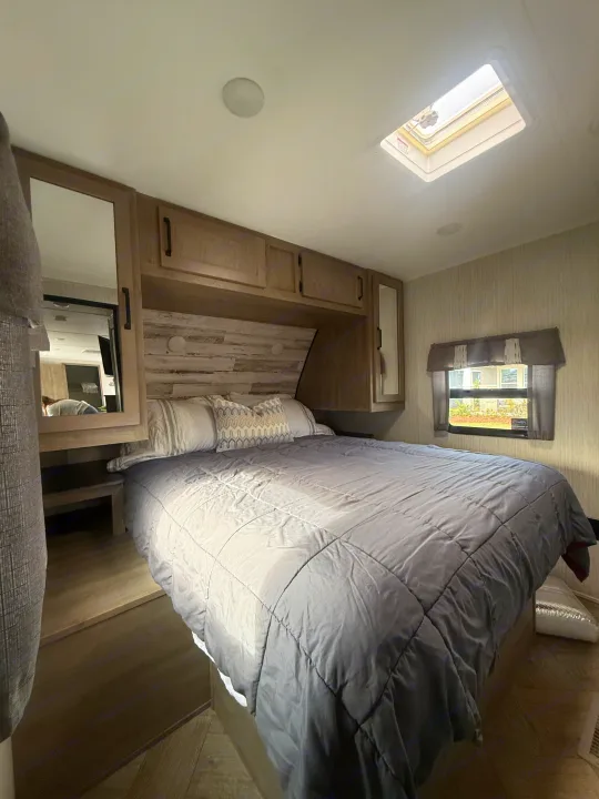 Comfortable RV rental bedroom with a cozy bed, overhead storage, side mirrors, a window with curtains, and a ceiling skylight.. Forest River Palomino Puma 2022