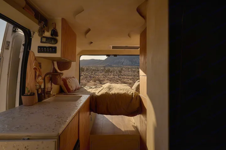 Cozy RV rental interior: A modern camper van with a bed, kitchen, and a desert view through the back window.. Dodge Ram 1500 2021