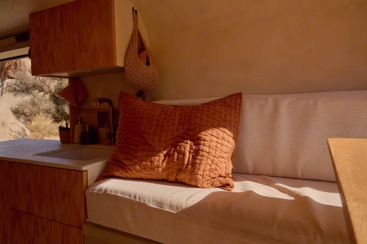 Cozy RV rental interior with a compact kitchen, comfy bench, and a terracotta pillow bathed in desert sunlight.. Dodge Ram 1500 2021
