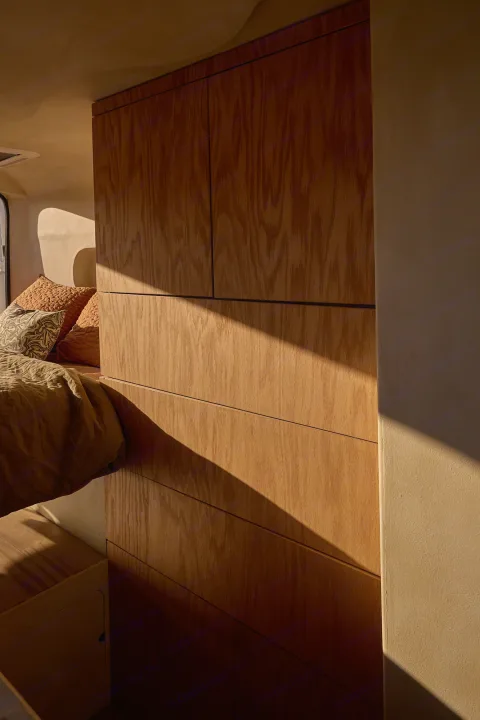 Sunlit RV rental interior with minimalist wood cabinets & cozy bed. Warm light casts diagonal shadows.. Dodge Ram 1500 2021
