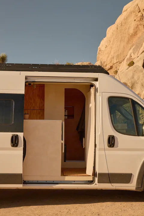 An open rv rental's custom interior, featuring wood and light-toned walls, is visible as it sits in a rocky desert landscape.. Dodge Ram 1500 2021