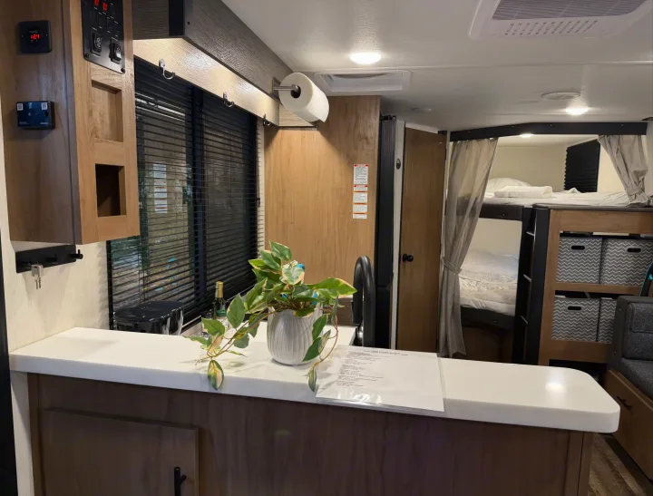Inside a well-appointed RV rental featuring a kitchen counter with a plant, bunk beds, and a functional control panel.. Forest River Campsite Reserve 2025