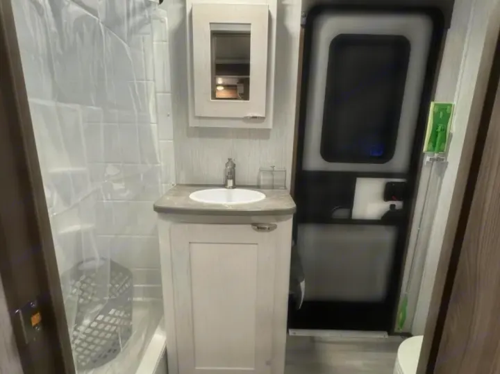 Compact rv rental bathroom: shower, sink vanity, medicine cabinet, and RV entrance door visible. Perfect for your trip.. Cruiser RV MPG 2023