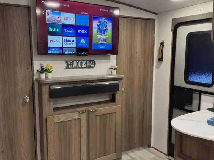 Enjoy an RV rental with a smart TV displaying streaming apps, soundbar, and "Into the Woods" sign. Cozy interior entertainment!. Cruiser RV MPG 2023