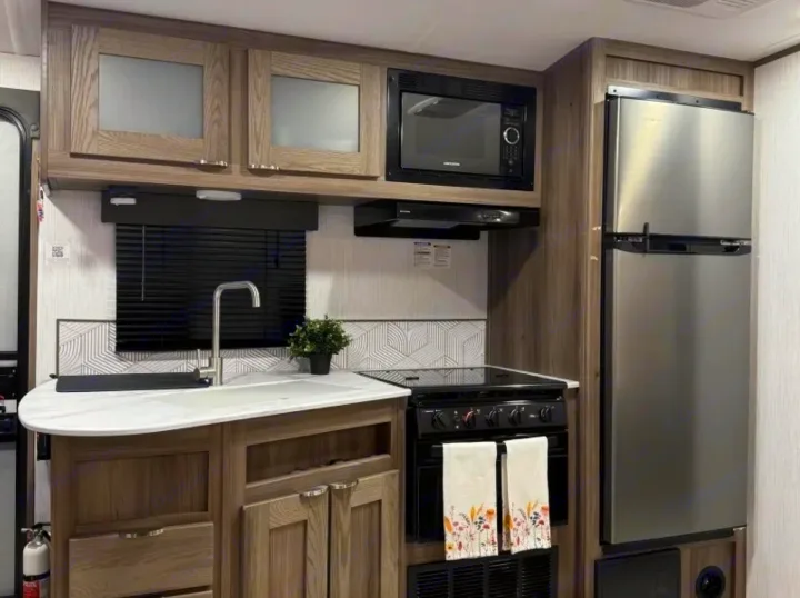 Modern RV rental kitchen with wood cabinets, stainless steel fridge, microwave, stove, sink, and stylish backsplash.. Cruiser RV MPG 2023