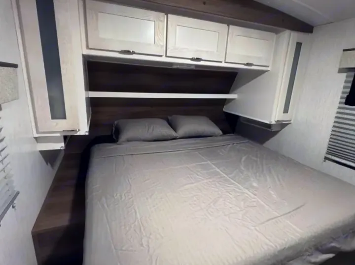 Explore this cozy RV rental bedroom featuring a full bed, overhead cabinets, and convenient bedside storage.. Cruiser RV MPG 2023