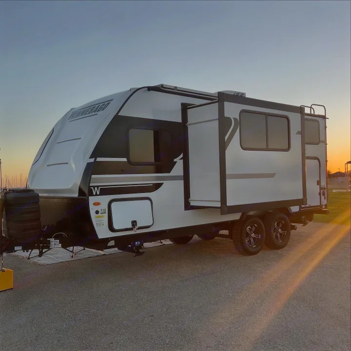 A white Winnebago travel trailer rv rental, with an extended slide-out, is parked at sunset. Perfect for outdoor adventure.. Winnebago Micro Minnie 2100BH 2025