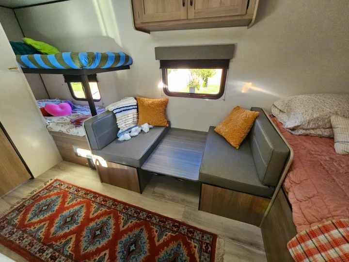 Cozy RV rental interior featuring bunk beds, a dinette, and a main sleeping area with a colorful rug.. Keystone Coleman 17BX 2025