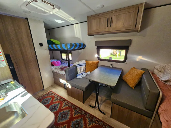 Cozy RV rental interior: dinette, bunk beds, kitchen, and warm lighting create a welcoming space.. Keystone Coleman 17BX 2025