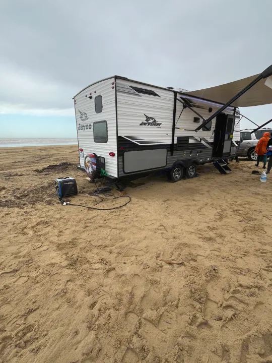 Jayco RV rental parked on a sandy beach with an extended awning and generator, under a cloudy sky.. Jayco Jay Flight SLX Rocky Mountain Edition 2022