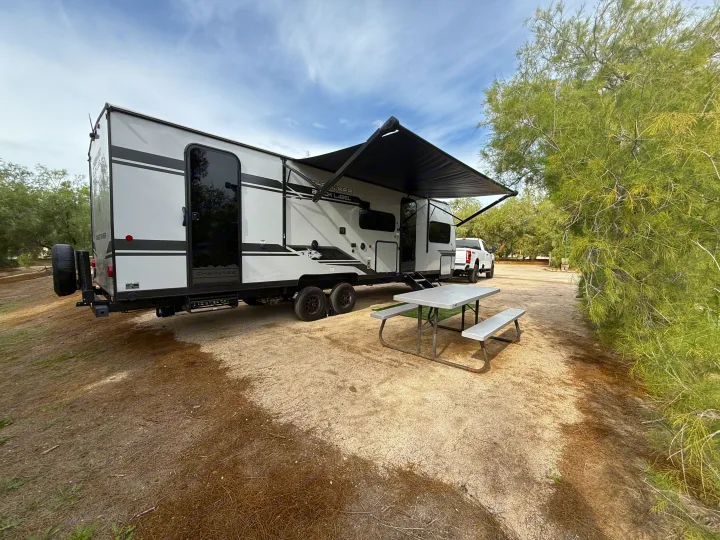 RV rental ready for adventure: a travel trailer with an extended awning, picnic table, and truck at a dusty campsite.. Forest River Grey Wolf Black Label 2026
