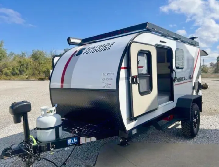 Compact white Bontrager Outdoors Radical teardrop camper, with open door, propane tank, and roof rack. Explore with this rv rental.. Bontrager Outdoors 12RAD 2025