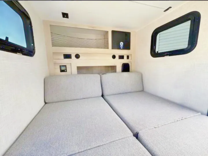 Compact rv rental interior: grey seating converts to beds, with built-in storage, windows, and control panels.. Bontrager Outdoors 12RAD 2025