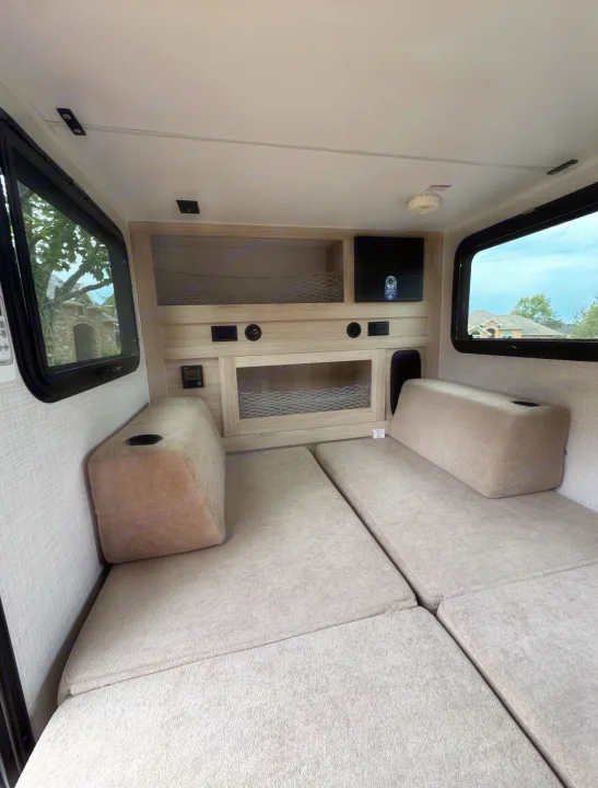 Cozy RV rental interior featuring light-colored convertible seating/beds, overhead storage, and windows on both sides.. Bontrager Outdoors 12RAD 2025