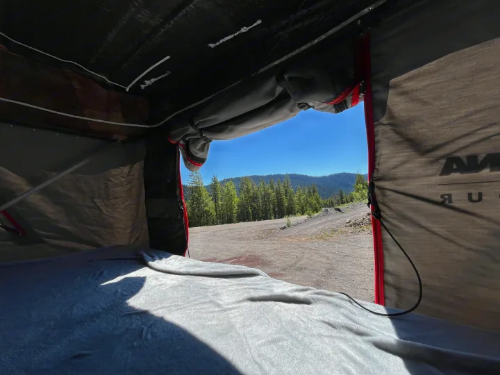 Inside a comfy RV rental rooftop tent, a bed offers views of a vast forest, rolling hills, and clear blue sky.. Chevrolet Astro Van 1997