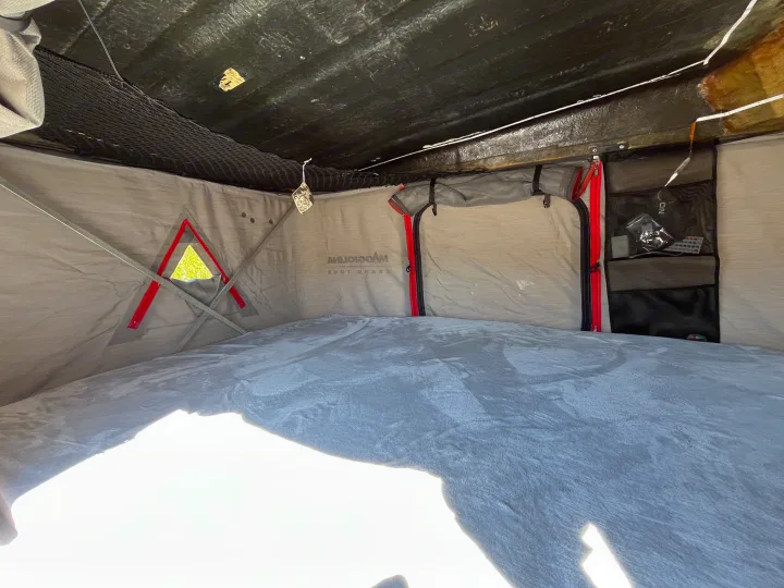 Interior of a cozy RV rental rooftop tent featuring a comfortable bed, storage, and natural light for camping adventures.. Chevrolet Astro Van 1997