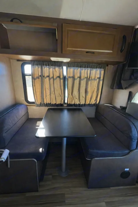 Interior of an **rv rental**: dinette with gray bench seating, a black table, and brown overhead cabinets.. Thor Majestic 2018