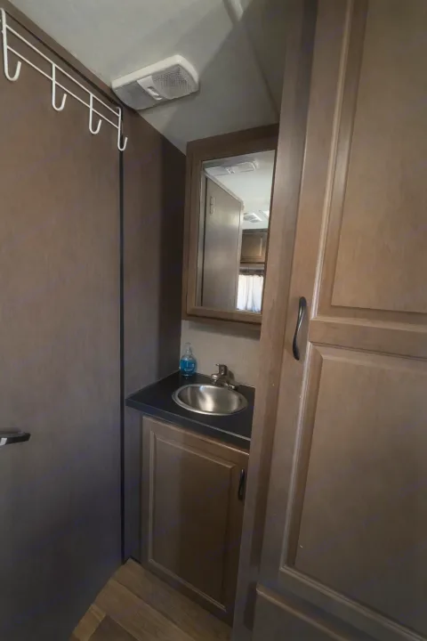 Compact RV rental bathroom featuring a sink, mirror, wooden vanity, and wall hooks for convenience.. Thor Majestic 2018
