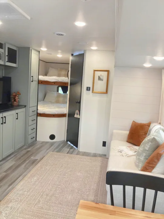 Bright RV rental interior: light wood floors, cozy bunk beds, soft sofa with pillows, and modern light grey cabinetry. Travel ready!. Jayco Jay Flight SLX 2025