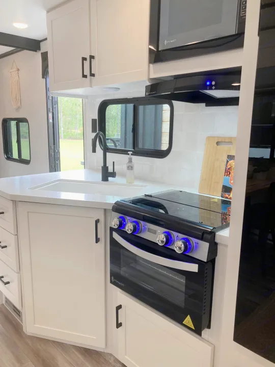 Clean RV rental kitchen with modern white cabinets, black hardware, sink, oven with blue lights, and microwave.. Jayco Jay Flight SLX 2025