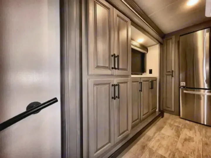 This modern RV rental interior features sleek grey cabinets, a stainless steel fridge, TV, and a safety handrail.. Keystone RV Montana 2023
