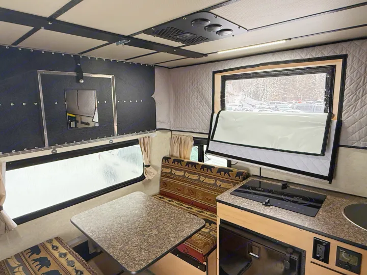 Experience this RV rental's cozy interior with a kitchenette, dining area, and insulated windows offering a snowy outdoor view.. Four Wheel Campers Hawk + 2026