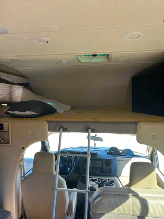 Cozy RV rental interior view from the living area, showcasing the cab-over bunk bed with ladder and the front cabin area.. Thor Freedom Elite 2021