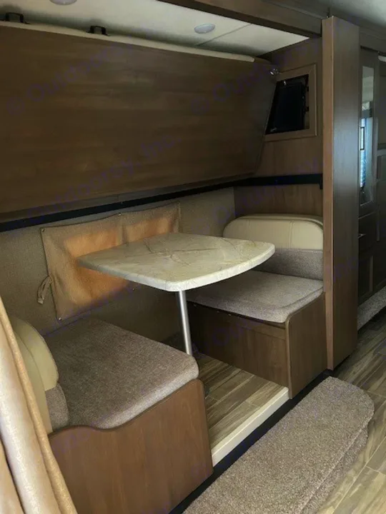 RV rental dinette with cushioned benches, a table, and an overhead fold-down bunk bed. A functional RV living space for travelers.. Thor Freedom Elite 2021