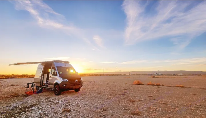An RV rental camper van parked in a wide-open desert, illuminated by the warm glow of a beautiful sunset. Perfect for outdoor adventures.. Winnebago Revel 2020