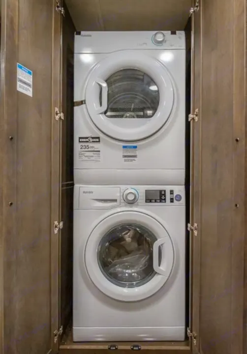 Stacked white washer/dryer in a wooden RV rental cabinet. Compact laundry appliance for travel convenience.. Georgetown GT7 2022