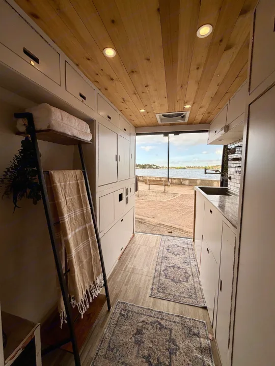 Cozy RV rental interior with wooden ceiling, white cabinets, and stunning waterfront view. Perfect for van life adventures!. Gmc Ram Promaster 2018