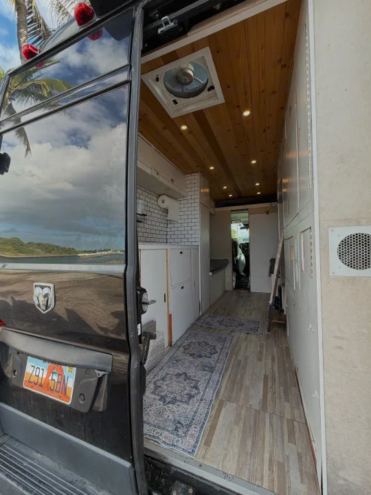 RV rental camper van interior. Wooden ceiling, kitchen, storage, and rugs, seen from the open back door with beach reflections.. Gmc Ram Promaster 2018