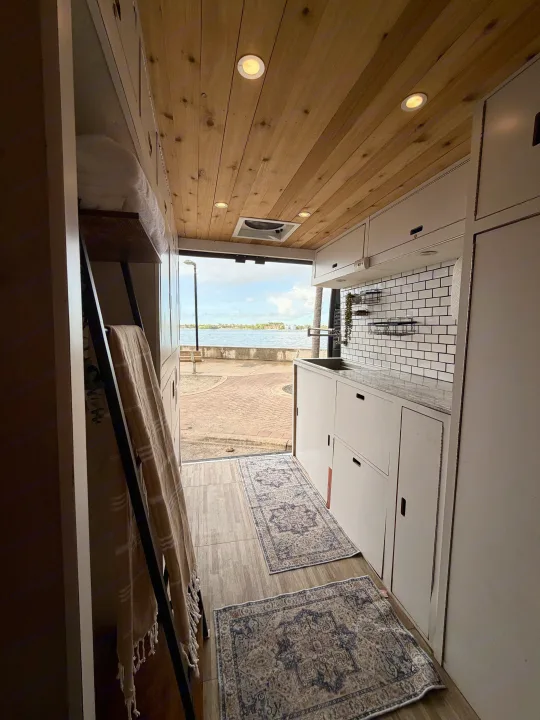 Enjoy this cozy camper van rental interior with a kitchenette, wood ceiling, patterned rugs, and a scenic waterfront view.. Gmc Ram Promaster 2018