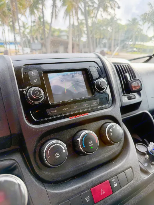 Inside an RV rental: dashboard with backup camera display, climate controls, and palm trees through the wet windshield.. Gmc Ram Promaster 2018