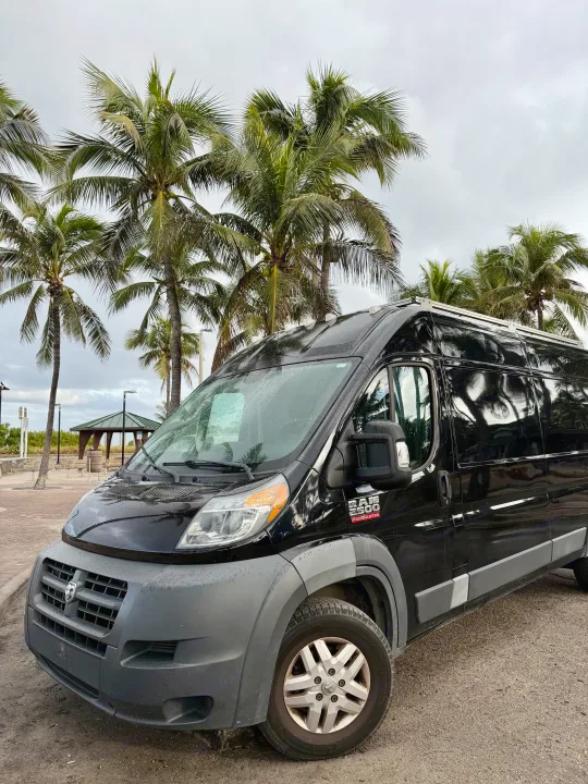 Black Ram ProMaster rv rental van parked by tropical palm trees under a cloudy sky, ready for a beach adventure.. Gmc Ram Promaster 2018