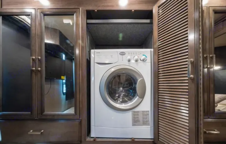 RV rental interior: A compact front-load washing machine in a dark wood cabinet, with mirrored and louvered doors.. Fleetwood Pace Arrow 35E 2019