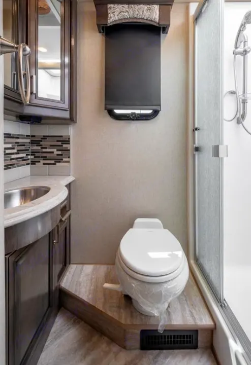 Compact RV rental bathroom showcasing a vanity, toilet on a raised platform, shower, and window. Ideal for road trips.. Fleetwood Pace Arrow 35E 2019