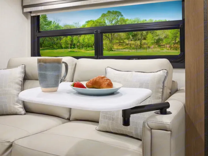 Enjoy serene mornings in this comfortable RV rental! Features a plush sofa, armrest table with breakfast, and a beautiful window view.. Axis 24.1 2027