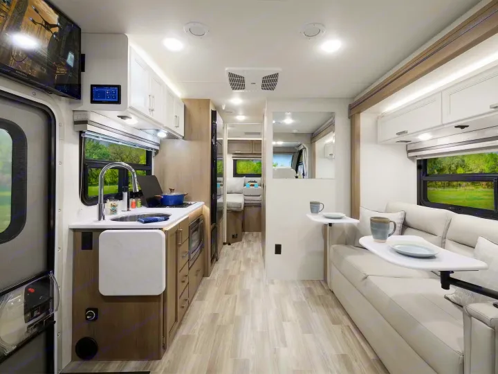 This bright rv rental interior features a modern kitchen, sofa seating with tables, and amenities for comfortable travel.. Axis 24.1 2027