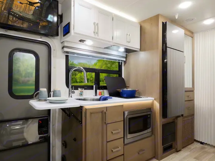 This modern RV rental features a compact kitchen with a sink, stovetop, microwave, and fridge, ideal for your next adventure.. Axis 24.1 2027