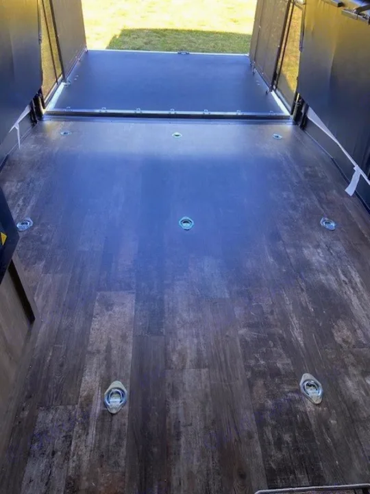 RV rental's cargo area floor features dark wood-look vinyl with multiple D-ring tie-downs for securing gear, leading to the open rear ramp.. Forest River Cherokee Wolf Pack 2021