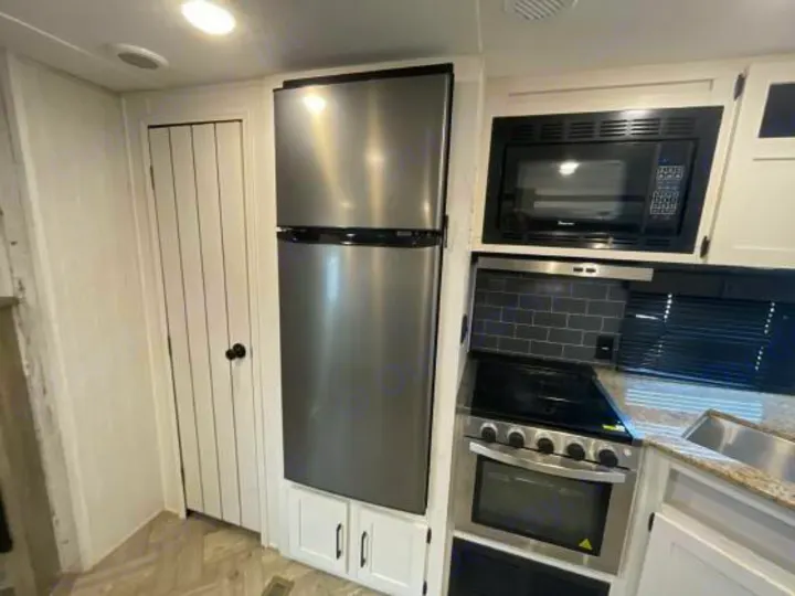 RV rental kitchen: stainless steel fridge, microwave, oven, & sink, with white cabinets & tiled backsplash.. Palomino 28bhss 2020