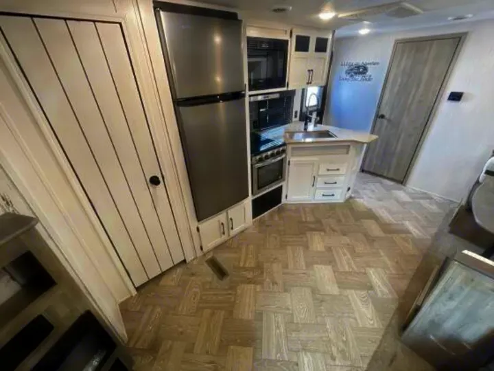 Bright RV rental interior showcasing a modern kitchen with stainless steel fridge, oven, and sink, plus white cabinets & patterned flooring.. Palomino 28bhss 2020