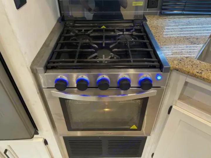 RV rental kitchen featuring a modern stainless steel gas range with a stovetop, oven, and blue illuminated control knobs for cooking.. Palomino 28bhss 2020