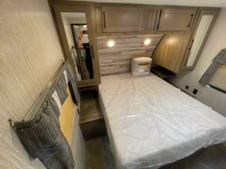 Comfortable **rv rental** bedroom featuring a plastic-covered mattress, overhead cabinets, and a side mirror. Ready for your trip.. Palomino 28bhss 2020