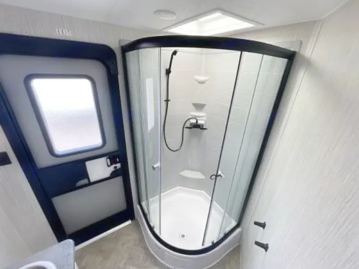 An RV rental compact bathroom with a modern corner glass shower and an entry door with a window, featuring white walls and floor.. Palomino 28bhss 2020