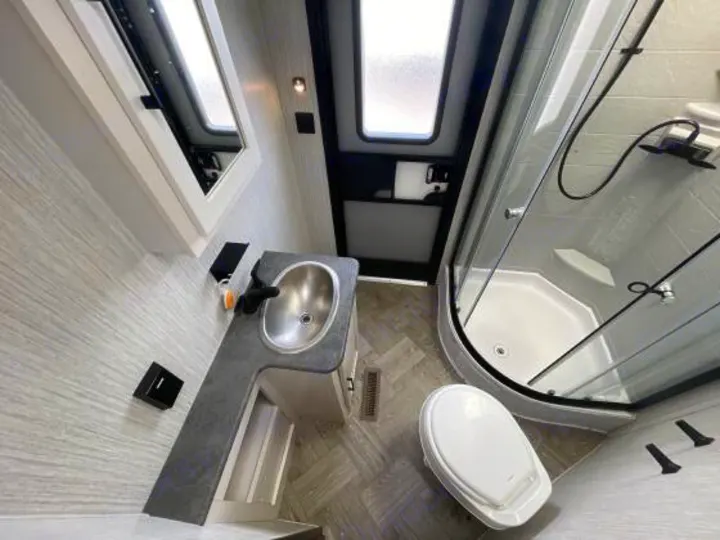 Modern RV rental bathroom featuring a sleek sink, mirror, clear glass shower, and white toilet.. Palomino 28bhss 2020